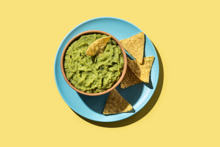 Mexican guacamole with nacho chips in wooden bowl on yellow backgroundの写真素材