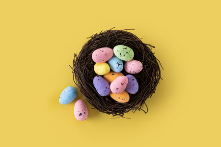 Colorful Easter eggs inside a nest on yellow backgroundの写真素材