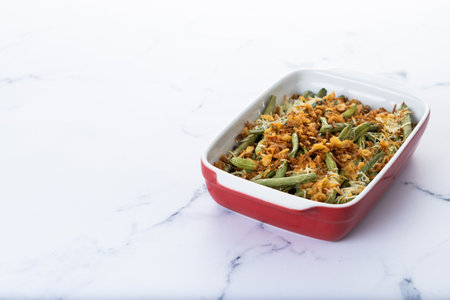 A traditional green bean casserole topped with French Fried Onions and cream of mushroom on white marble. close upの写真素材