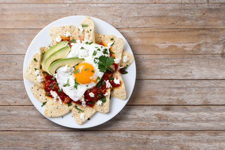 Traditional Mexican breakfast red chilaquiles with egg on wooden tableの写真素材