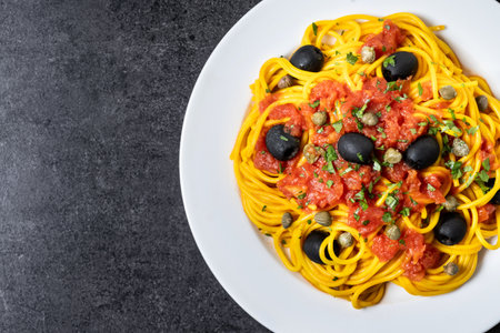 Italian Pasta puttanesca with tomato sauce, capers, and black olives on black slate backgroundの写真素材