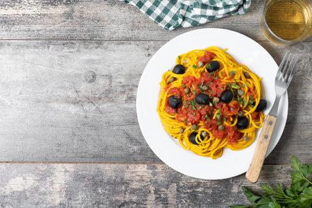 Italian Pasta puttanesca with tomato sauce, capers, and black olives on wooden tableの写真素材