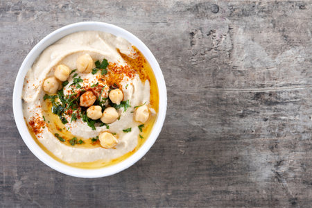 Chickpea hummus with olive oil, parsley and paprika in bowl on wooden tableの写真素材