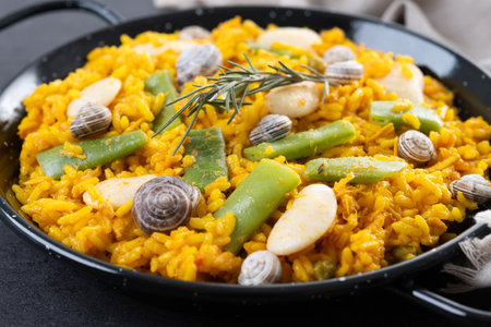 Traditional Valencian paella with rabbit, chicken, garrofon beans, snails, Moroccan green beans and saffron on black background.の写真素材