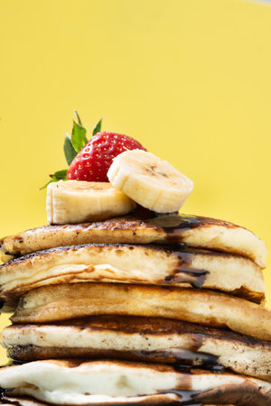 Pancakes with chocolate, strawberry and banana on yellow background
