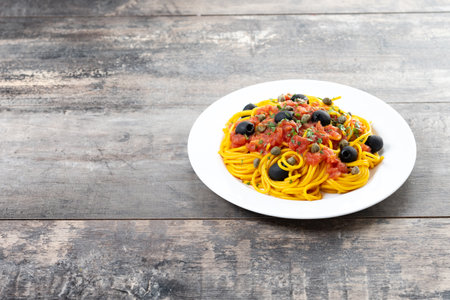 Italian Pasta puttanesca with tomato sauce, capers, and black olives on wooden tableの写真素材