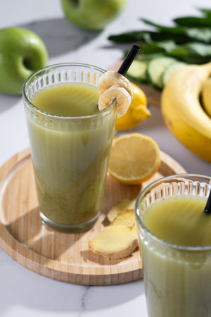 Green smoothie with spinach, banana, apple, and lemon on white marbleの写真素材