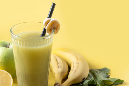 Green smoothie with spinach, banana, apple, and lemon on yellow backgroundの写真素材