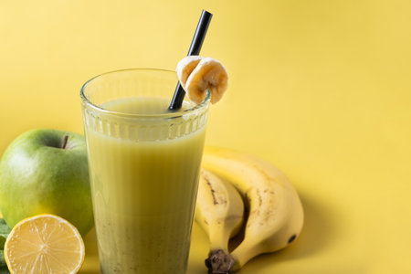 Green smoothie with spinach, banana, apple, and lemon on yellow backgroundの写真素材