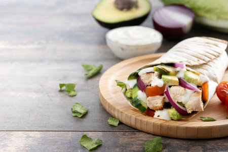 A delicious grilled chicken wrap with vegetables and avocado on wooden tableの写真素材