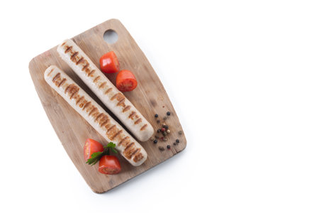 Grilled Bratwurst sausages with cherry tomatoes on a wooden cutting boardの写真素材