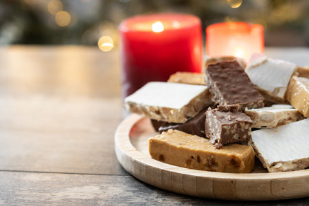 Assorted traditional Christmas nougat on wooden plate with candles in backgroundの写真素材