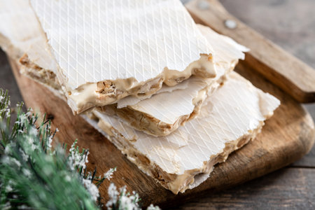 Traditional Christmas sweet, pieces of delicious almond nougat on wooden table (hard nougat)