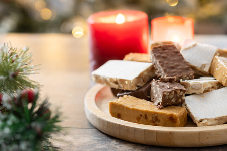 Assorted traditional Christmas nougat on wooden plate with candles in background