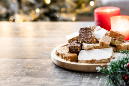 Assorted traditional Christmas nougat on wooden plate with candles in background