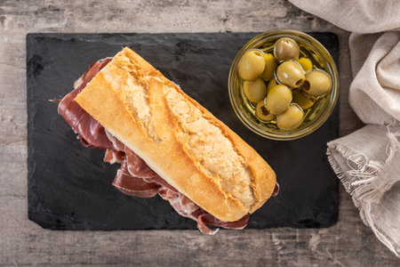 Close-up of a Serrano ham sandwich made with crusty baguette bread, placed on wooden table