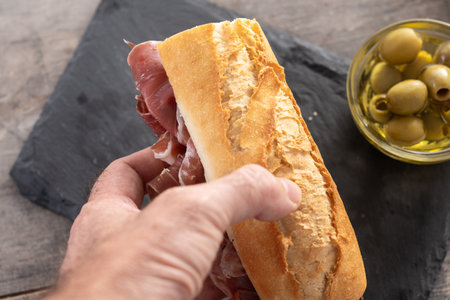 Hand Holding Spanish Serrano Ham Sandwich on wooden background