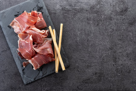 Slices of Serrano Ham on black slate background