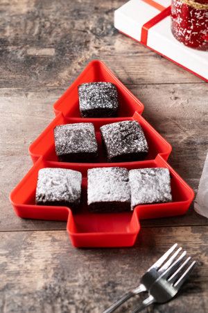 Chocolate brownies with powdered sugar in Christmas tree tray on wooden tableの写真素材