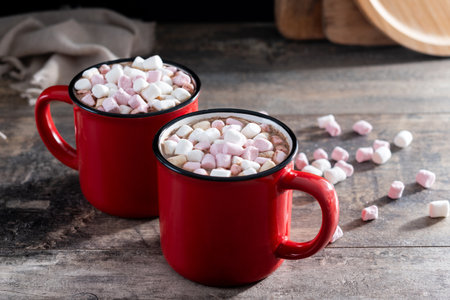 Hot chocolate drink with marshmallows in red mug on wooden table