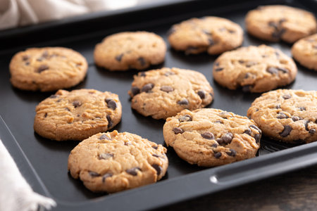 Close-up of homemade chocolate chip cookies cooling on a black baking tray.