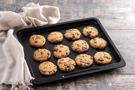 Close-up of homemade chocolate chip cookies cooling on a black baking tray.