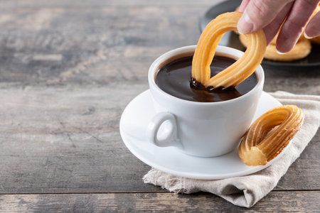 Spanish churros with hot thick chocolate in a white cup on wooden tableの写真素材