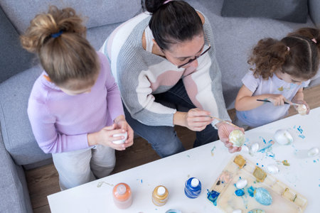 Mother and two daughters painting Easter eggs at home.