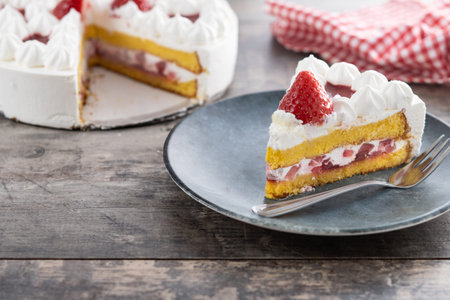 Slice of strawberry cake with fresh strawberries on wooden table