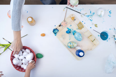 Mother and daughter painting Easter eggs at home.