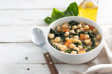Homemade chickpea and spinach soup with sliced carrots served in a white bowl on wooden tableの写真素材