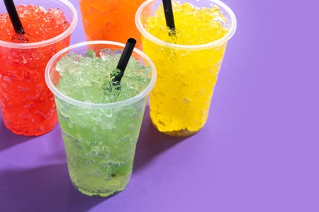 Colorful Frozen Slush Drinks in Plastic Cups on Purple Background