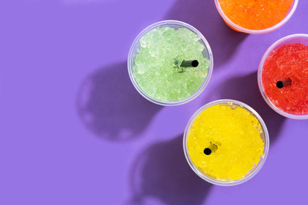 Colorful Frozen Slush Drinks in Plastic Cups on Purple Background