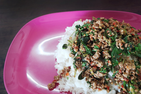 Fried rice with basil in a plastic pink plate on a wooden table,Concept Spicy foods that should not be used in certain types of containers.の写真素材