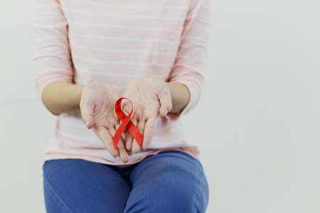 Asian woman with pink shirt is showing red ribbon (Aids symbol) on white isolatedの写真素材