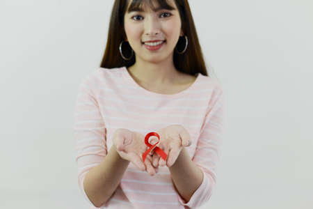 Asian woman with pink shirt is showing red ribbon (Aids symbol) on white isolatedの写真素材