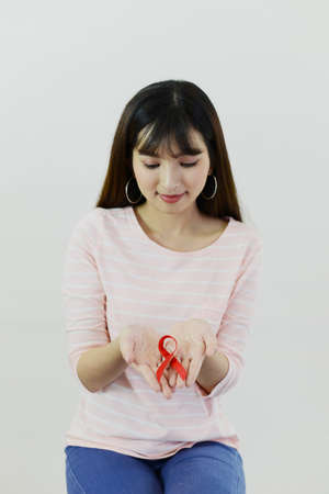 Asian woman with pink shirt is showing red ribbon (Aids symbol) on white isolatedの写真素材