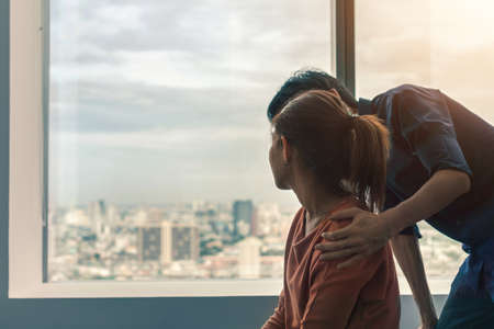 PTSD Mental health concept, Psychologist sitting and touch young depressed asian woman for encouragement near window with low light environment.Selective focus.の写真素材