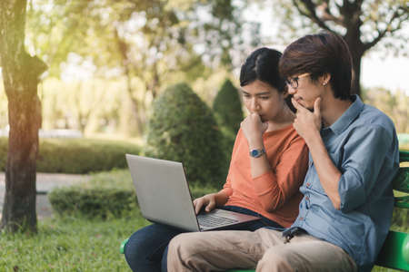 Young business asian man and woman working with laptop and thinking about online business on bench...