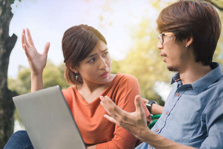 Young business asian man and woman working with them laptop and talking serious  on a bench in the park outdoors on vacation time.の写真素材