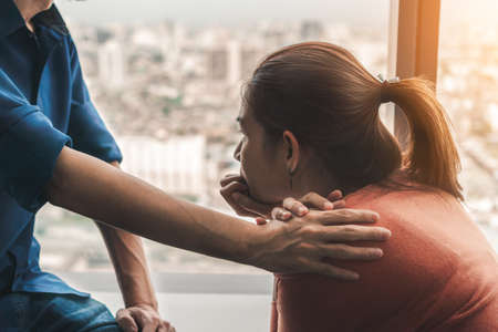 Psychologist sitting and touch young depressed asian woman for encouragement near window with low light environment, Selective focus, PTSD Mental health concept,の写真素材