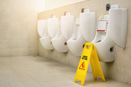 Out of service of Urinal pot with yellow sign warning caution wet floor or cleaning in progress in toilet. Out of service of Urinal pot with yellow sign warning caution wet floor or cleaning in progress in toilet.