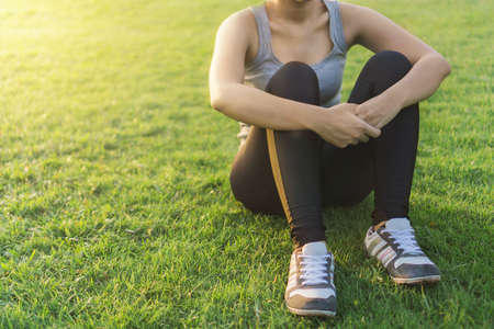 Exercise and healthy concept, Young asian woman runner sitting on green grass to relax after jogging in the park at morning time, selective focusの写真素材