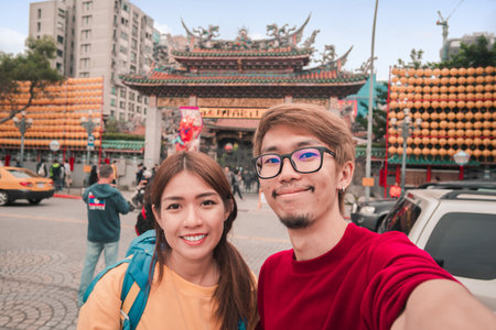 Asian man and woman traveler with backpack standing take photo selfie at Longshan Buddhist temple, landmark temple in taiwan.の写真素材