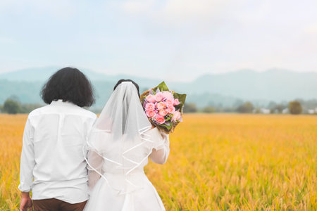 Bride and groom lovely couple hold of hands and hold flower at meadow outdoor location, copy space.の写真素材