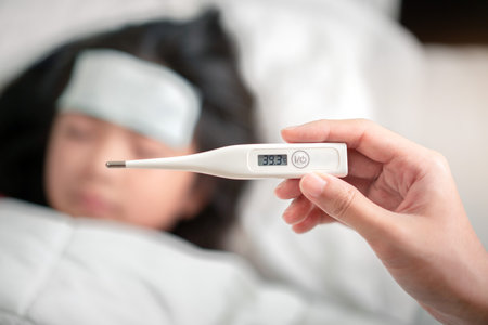 Asian mother holding digital thermometer  with high temperature for check health her daughter, Sick child have cool towel for reduce high fever, Hand focus, Healthy and infection conceptの写真素材