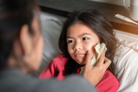 Asian mother take cool towel for reduce high fever on sick girl forehead on bed at morning time,Sick...
