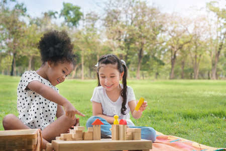 Happy cheerful ethnic girls play wooden block puzzle together at outdoors park , Relationship little...