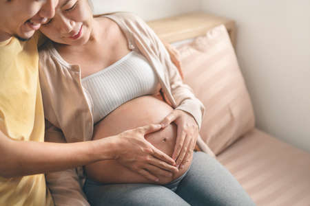 Asian pregnant woman and husband embrace and making hand heart gesture on her belly,  Expectation of a child and Maternity prenatal care and woman pregnancy concept.の写真素材