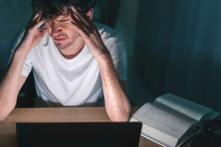 Depressed caucasian man losing job and heartbroken at same time sitting alone on sofa with low light...